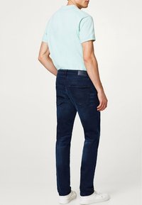 Ljusblå polo-shirt och mörkblå jeans med slim fit. Jeansen har två bakfickor och en strukturerad midja. Vita sneakers.