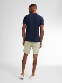 Námorně modré tričko s krátkým rukávem, v kombinaci se světle khaki šortkami a bílými teniskami. Jednoduchý design, bavlněný materiál a volný střih.