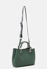 Zelená texturovaná kabelka s dvojitými uchy a odnímatelným černým popruhem, který má bílé logo. Stříbrné kovové prvky dotvářejí design.