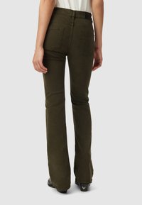Flared olive green pants with a fitted waist, two back pockets, and smooth texture, styled with black footwear.