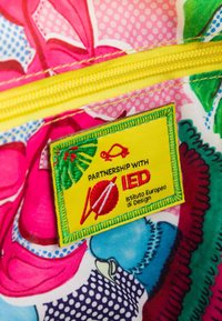 Tela multicolor con patrones florales, lunares y un bolsillo con cremallera amarillo que tiene una etiqueta de asociación verde y roja para IED.