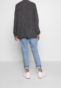 Pull en maille gris surdimensionné avec épaules tombantes, porté par-dessus un jean bleu clair retroussé et des baskets blanches. Texture douce, coupe décontractée.