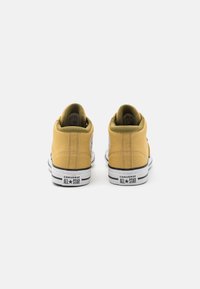 Žluté plátěné vysoké tenisky s bílými gumovými podrážkami, kontrastními černými pruhy a značenými patami s nápisem "CONVERSE ALL STAR."