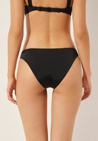 Black bikini bottom with a smooth, glossy texture, low-rise design, and moderate coverage at the back, featuring high-cut leg openings.