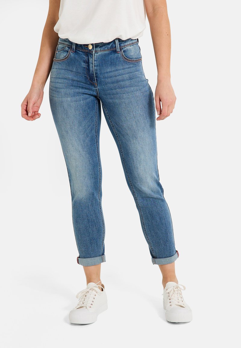 Jean en denim bleu avec une taille haute, des jambes fuselées, des ourlets retroussés, cinq poches et des détails de couture contrastants. Associé à des baskets blanches.