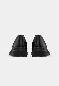 Black leather shoes with a smooth finish, low heel, and rounded shape. Features rounded edges and a minimalistic design with no visible hardware.