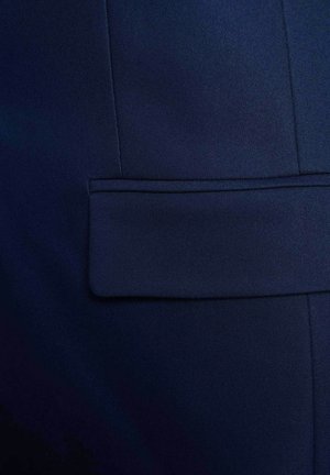 Giacca blu scuro su misura con tasca a pattina orizzontale e cuciture verticali visibili su tessuto liscio.