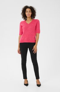 Pull rose à col en V et à manches courtes en tissu doux, porté avec un jean skinny noir et des escarpins noirs à bout pointu.