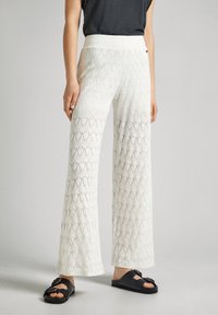 Pantalones de punto blancos con un patrón en zigzag, de pierna ancha y una cinturilla suave, combinados con sandalias negras con una hebilla decorativa.
