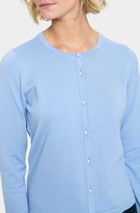 Cardigan bleu clair en tricot doux et côtelé. Présente un col rond et des boutons sur le devant, chacun orné de petites perles.