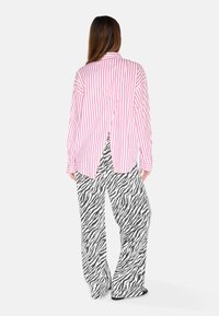 Striped pink and white long-sleeve shirt with a back slit, paired with black and white zebra print wide-leg pants.