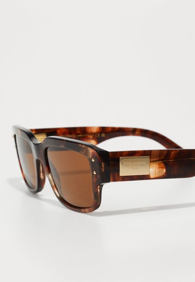 Tortoiseshell sunglasses with brown lenses, thick frames, and a gold logo plaque on the temple. Brown gradient color pattern throughout.