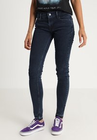 Mörkblå skinny jeans i denim med medelhög midja, fem fickor och en ren design. Bärs med lila sneakers.