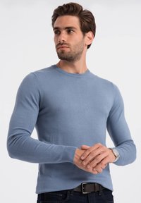 Lichtblauwe, lange mouwen trui van zacht gebreid materiaal, met een ronde hals, geribbelde manchetten en een slim fit ontwerp. Draag met een horloge en riem.