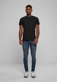 Camiseta de algodón negra con escote redondo, combinada con jeans de mezclilla azul ajustados con ligero desgaste y zapatillas blancas con detalles negros.