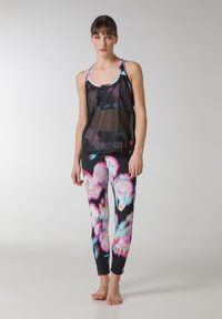Sort mesh tanktop lagd over et farverigt blomsterdesign leggings med pink, blå og sorte nuancer; tætsiddende design, velegnet til aktivt tøj.