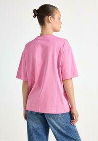 Lyserød bomuld t-shirt med korte ærmer, afslappet pasform, rund halsudskæring og blød tekstur; båret med blå, løstsiddende jeans.