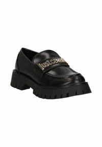 Mocassini in pelle nera con una larga fascia con lettering dorato. Suola nera spessa con scanalature distintive. Texture liscia e finitura lucida.