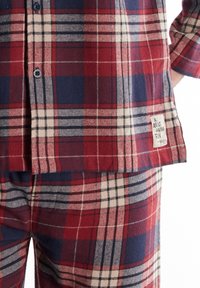 Rood en marineblauw geruit flanellen pyjamastel met knoopsluiting en een etiket met de tekst "Alles draait om plezier"; zachte textuur en relaxte pasvorm.