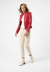Röd läderjacka med en figurnära design,beige byxor och ankelstövlar. Slät yta, dragkedja framtill och sidofickor.