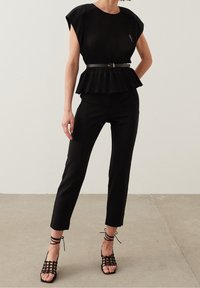 Top peplum plissé noir à manches courtes, associé à un pantalon noir slim et des sandales à talons noirs avec lanières. Design élégant et ajusté.