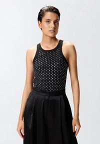 Top nero senza maniche dal design aderente, caratterizzato da un motivo di borchie argentate sul davanti, abbinato a pantaloni neri in satin a vita alta.