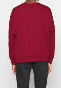 Sudadera burdeos de tela suave, con un ajuste relajado, hombros caídos y puños y dobladillo acanalados. Diseño simple sin patrones.