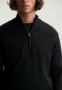 Pulover negru cu fermoar la gât, dintr-un material moale. Are un guler înalt cu un fermoar scurt. Textură netedă și design slim fit.