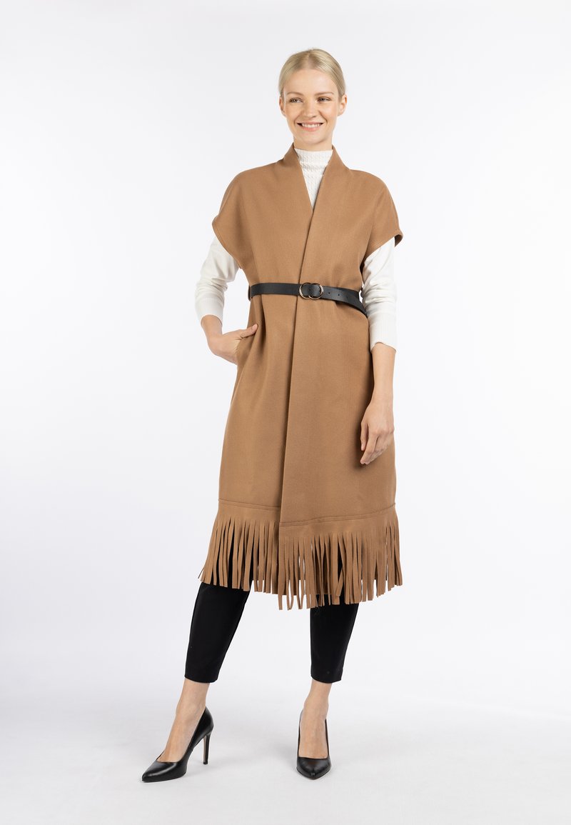 Gilet marrone con frange e cintura, realizzato in un tessuto texturizzato. Presenta un design aperto sul davanti ed è abbinato a una maglietta bianca a maniche lunghe.
