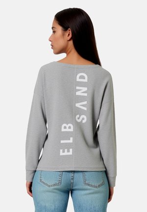 Light gray sweatshirt with a boat neck, long sleeves, and a relaxed fit. Features vertical white text on the back. Paired with blue jeans.