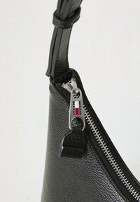 Sort tekstureret lædertaskehjørne med sølvlynlås og trækflap med rød, hvid og blå Tommy Jeans-logo.