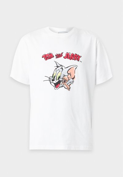 T-shirt blanc à manches courtes avec des visages de dessin animé de Tom le chat et Jerry la souris, avec le texte "Tom et Jerry" en rouge au-dessus.