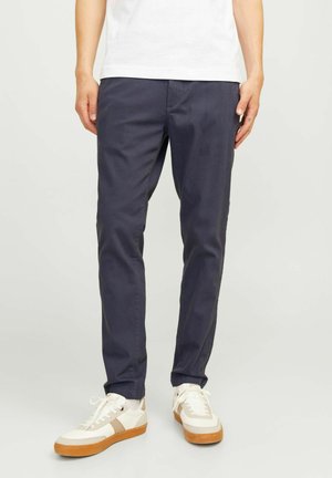 Marineblaue Chinos aus Baumwollmischung mit Slim Fit, ausgestattet mit Seitentaschen und zulaufenden Beinen, kombiniert mit weißen Sneakers.