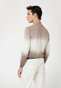 Beige és fehér gradiens pulóver puha kötésből, kerek nyakkal, hosszú ujjal, fehér farmerrel párosítva. Diszkrét textura, letisztult dizájn.