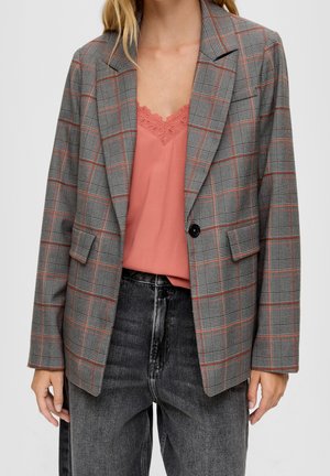 Personne portant un blazer à carreaux gris avec des lignes rouges, un caraco rose à bordure en dentelle et un jean noir délavé taille haute. Partie supérieure du corps visible.