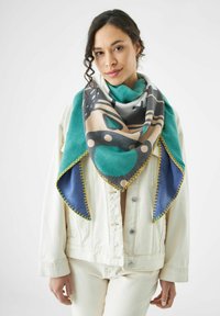 Écharpe multicolore avec un motif géométrique, présentant des teintes de canard, beige, gris et bleu. Bordée de coutures jaunes, fabriquée en tissu doux.