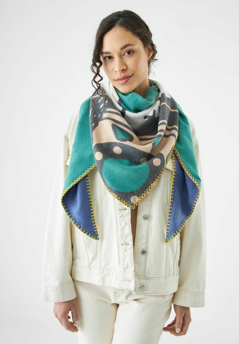Écharpe multicolore avec un motif géométrique, présentant des teintes de canard, beige, gris et bleu. Bordée de coutures jaunes, fabriquée en tissu doux.