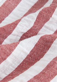 Gros plan sur un tissu froissé avec des larges rayures horizontales rouges et blanches alternées et un tissage texturé.