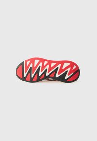 Suola della scarpa con colori rosso, nero e bianco. Presenta un motivo a zigzag per la trazione. Aree testurizzate nere e dettagli in rilievo.