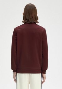 Felpa bordeaux con una texture liscia, polsini a coste e vestibilità rilassata, caratterizzata da un design minimalista e senza marchi visibili.