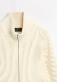 Cream-colored ribbed knit sweater with a silver front zipper and a high folded collar, labeled Massimo Dutti, made of cotton.