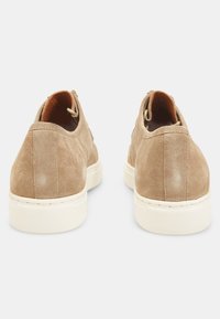 Tenisi bej din suede, cu o textură netedă, talpă din cauciuc alb și un design minimalist. Prezintă cusături contrastante și o buclă în spate.