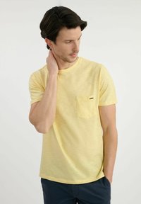 Żółta koszulka z krótkim rękawem z kieszonką na klatce piersiowej, wykonana z teksturowanej, lekkiej tkaniny. Projekt jest prosty, z okrągłym dekoltem.