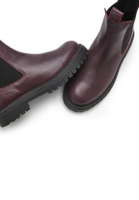 Burgundy leather ankle boots with elastic side panels, black rubber soles featuring a textured tread, and contrasting red stitching accents.