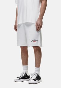 Witte katoen shorts met een losse pasvorm, met in zwart en rood geborduurde tekst "GOODFORNOTHING". Gecombineerd met zwarte sneakers en witte sokken.