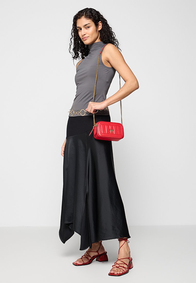 Haut sans manches gris, jupe asymétrique noire, sac à main matelassé rouge et sandales rouges à lanières, présentant une texture lisse et une silhouette élégante.