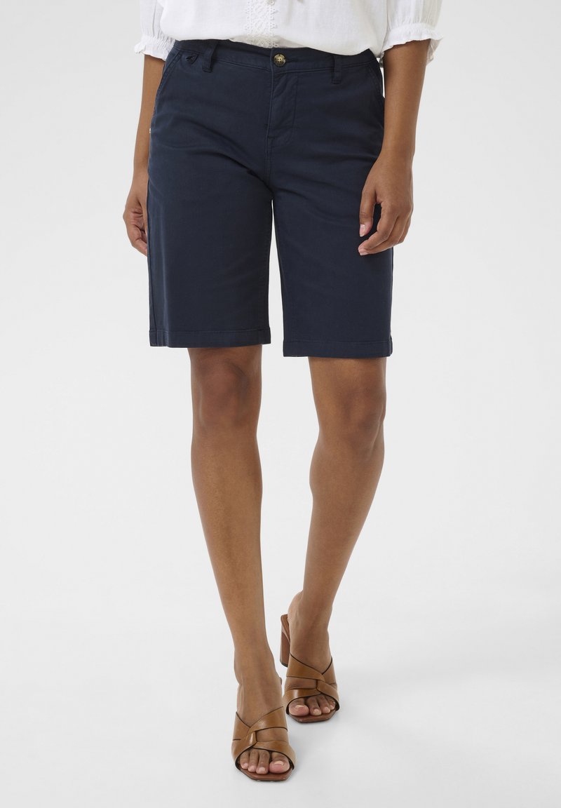 Mörkblå bomullsshorts med rak skärning, med framknäppning och uppvikta fållar. Kombineras med bruna klacksandaler.