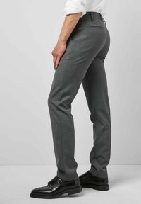 Schlanke graue Hose aus glattem Stoff, mit flachem Vorderteil, schmalem Bein und Gesäßtaschen. Kombiniert mit glänzenden schwarzen eleganten Schuhen.