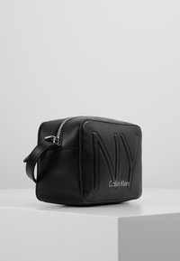 Borsa cosmetica in pelle nera di forma rettangolare, con loghi in rilievo "NY" e "Calvin Klein", chiusura con zip e manico laterale.