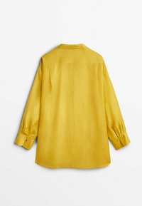 Chemise jaune à manches longues avec poignets boutonnés vue de dos sur fond blanc.